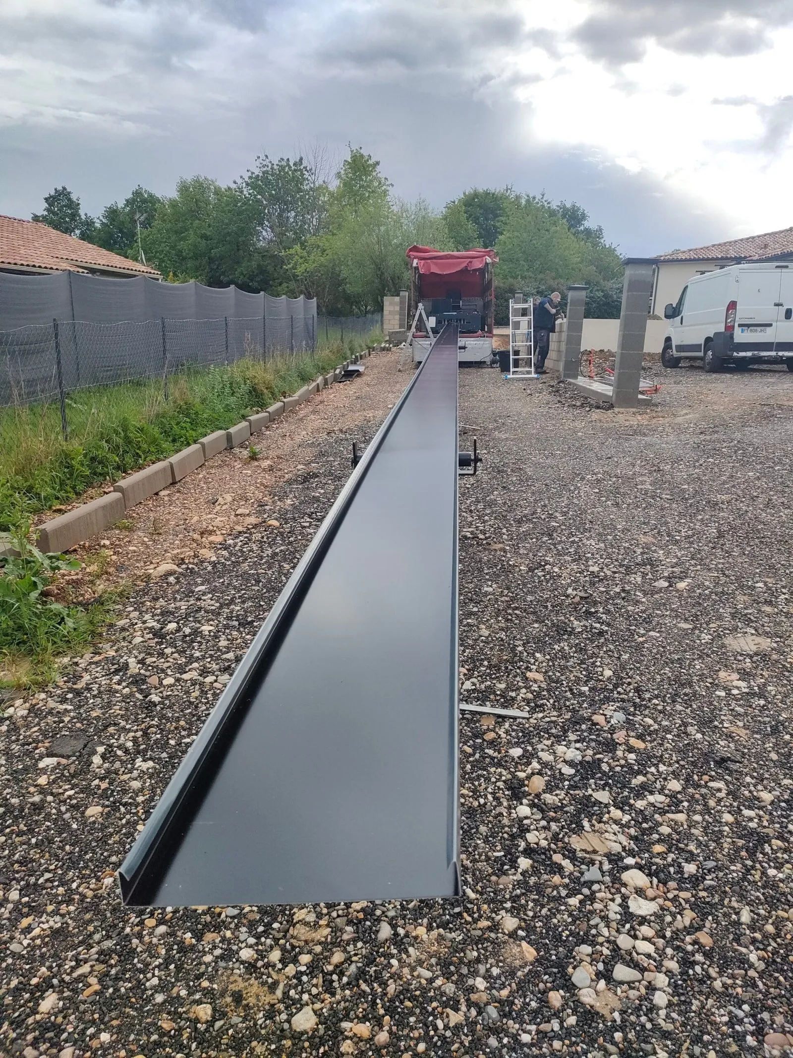 Longue couvertine en aluminium gris en cours de fabrication sur un chantier, avec l’atelier mobile en arrière-plan.