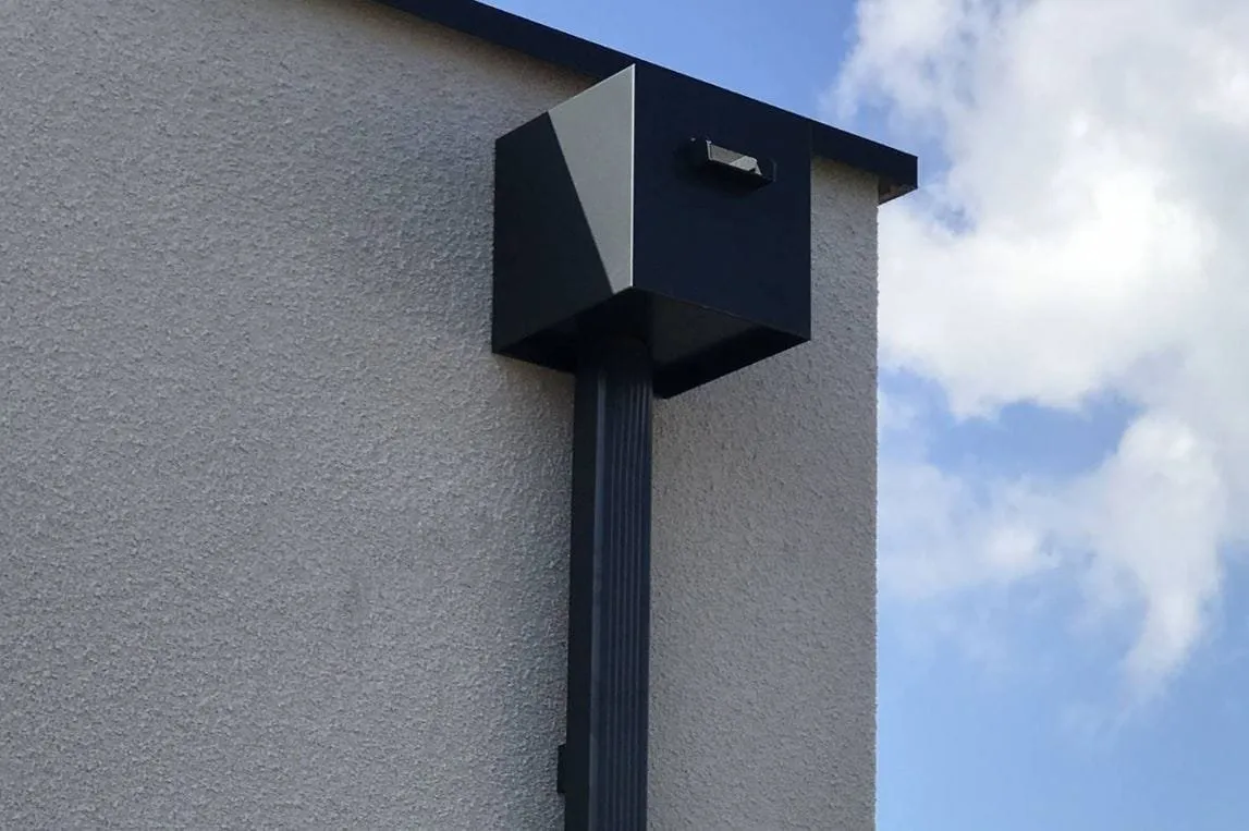 Boîte à eau gris anthracite et descente pluviale fixées sur la façade d'une maison.