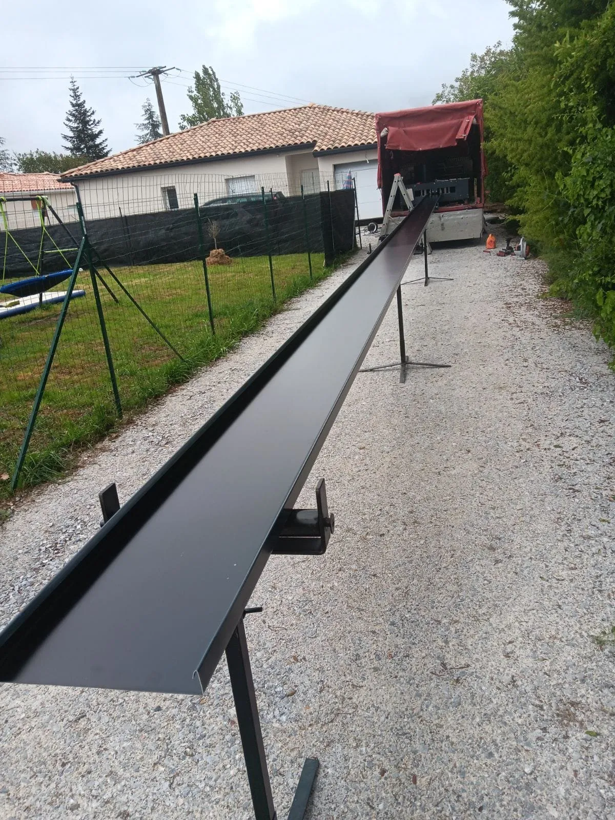 Long profil de couvertine en aluminium gris anthracite posé sur des tréteaux devant une maison.