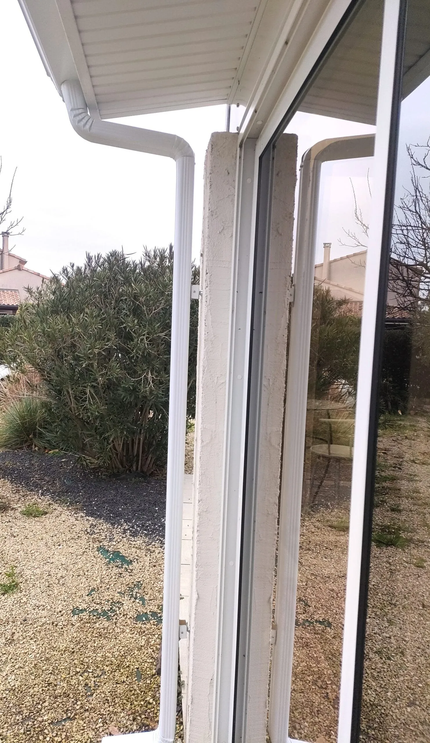 Descente de gouttière en aluminium blanc installée sous l’avancée de toit d’une véranda.