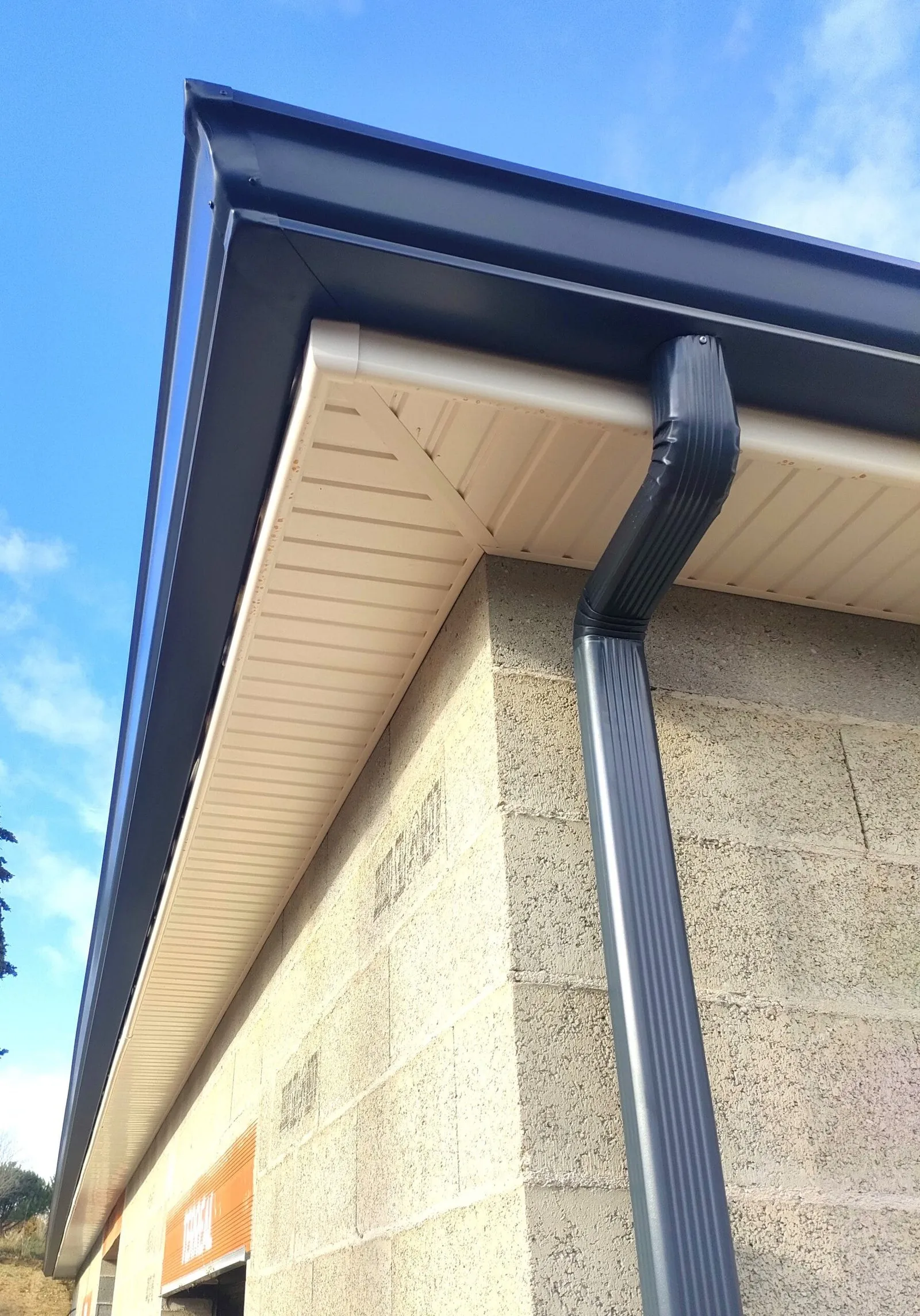 Gouttière et descente pluviale gris anthracite sur une maison avec sous-toiture blanche.