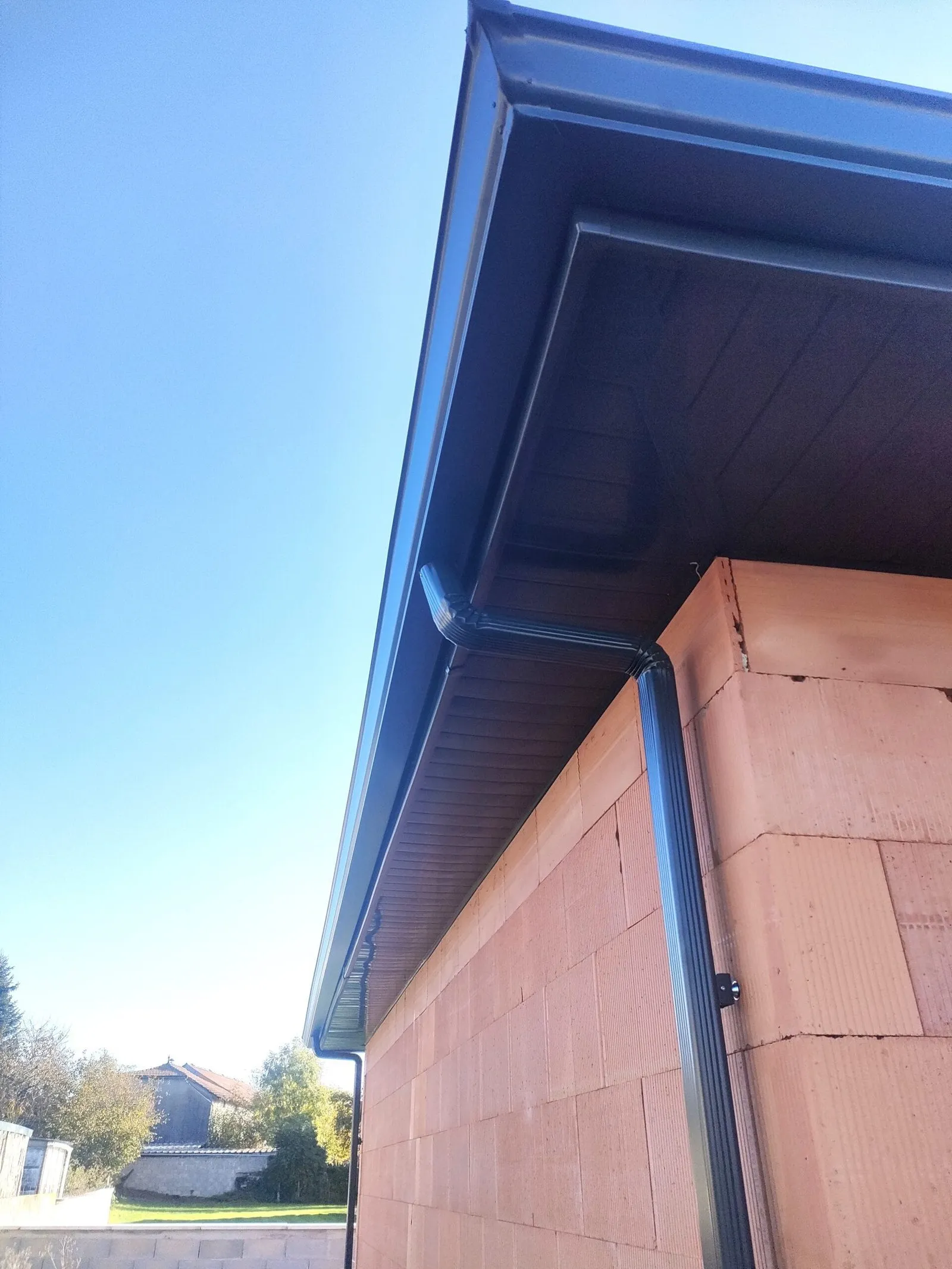 Gouttière et descente pluviale gris anthracite installées sous l’avancée d’une maison en briques.