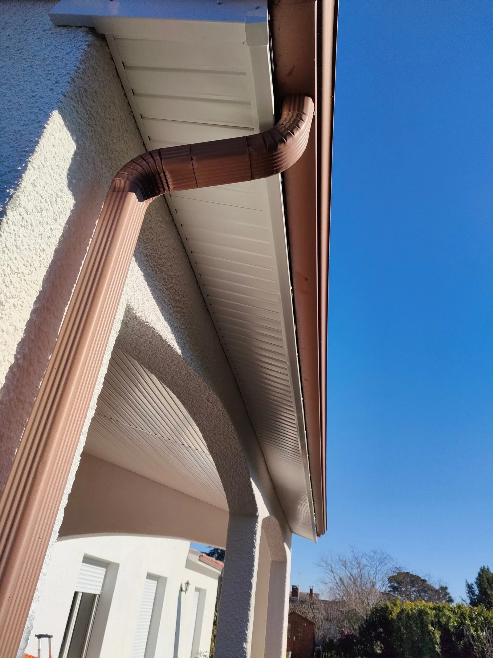 Descente de gouttière brune et lambris blanc sous l'avancée de toit d'une maison.